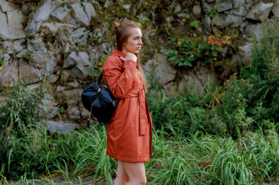 Portrait of young woman holding bag while standing on grassy field