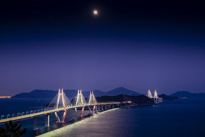 Illuminated bridge over sea against clear sky at night