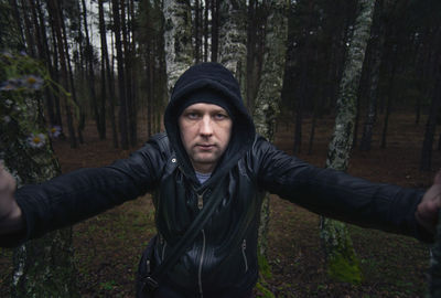 Portrait of woman standing by tree trunk in forest