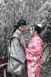 Side view of young couple standing against trees