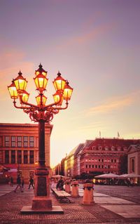 Illuminated street light in city against sky at sunset