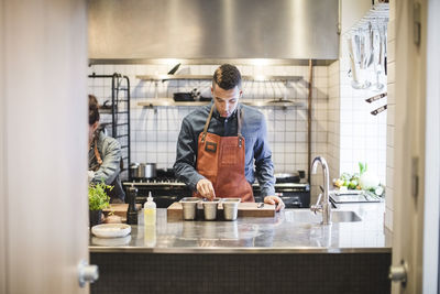Male chef preparing food at kitchen counter by female colleague in restaurant