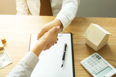 Midsection of real estate agent shaking hand with client at office