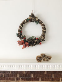 Christmas wreath hanging by pine cones on white wall at home