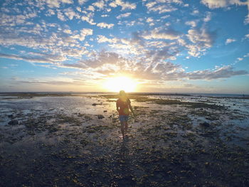 Rear view of woman at beach against sky during sunset