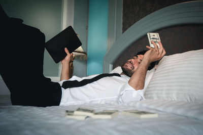 Midsection of man using mobile phone while relaxing on bed at home
