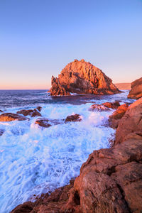 Rock formations on shore against clear sky