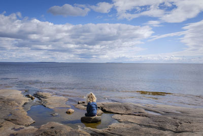 Toddler sitting on rocks looking out at water 