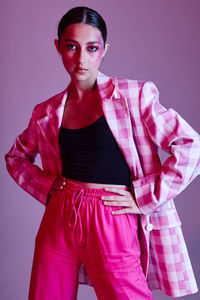 Portrait of young woman standing against pink background