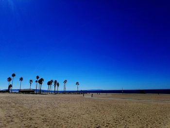 People on beach against clear blue sky