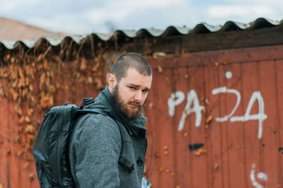 Close-up portrait of man standing against corrugated iron