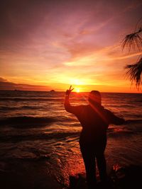Rear view of woman gesturing peace sign at beach during sunset