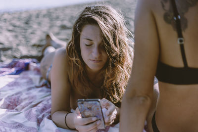 Midsection of woman by friend using mobile phone at beach