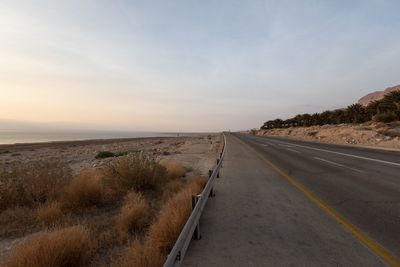 Road by sea against sky during sunset