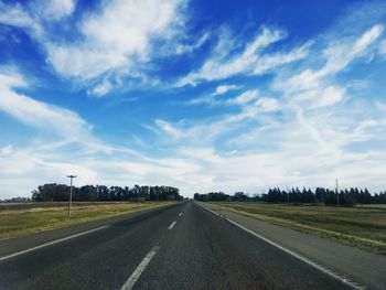 Empty road amidst field against sky