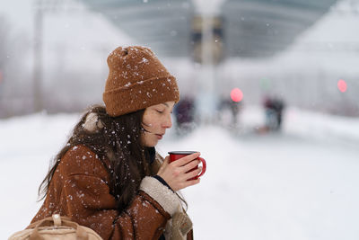 Traveler woman drinking hot tea travelling during cold winter waiting for train at outdoor platform