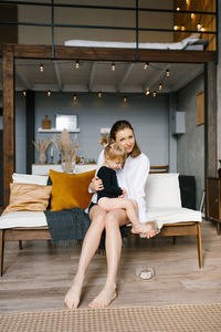 Young mom hugs her little daughter while sitting on the couch