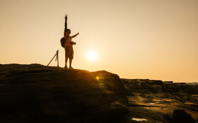 Silhouette person standing on rock against sky during sunset