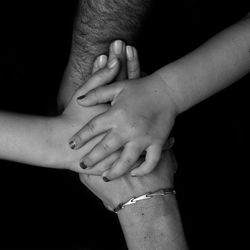 Cropped image of family stacking hands over black background