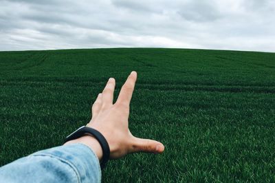 Cropped hand of person reaching sky over grassy field