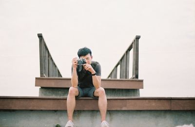 Full length of man photographing while sitting on metal