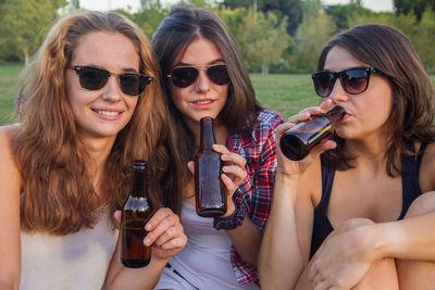 Portrait of young women drinking alcohol while sitting on field