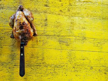 Directly above view of knife in grilled chicken on yellow table