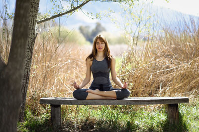 Mid adult woman with eyes closed meditating while sitting on bench amidst plants at park