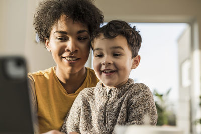 Smiling woman using digital tablet while sitting with boy at home