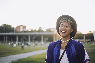 Portrait of cheerful young man with curly hair wearing hat at park