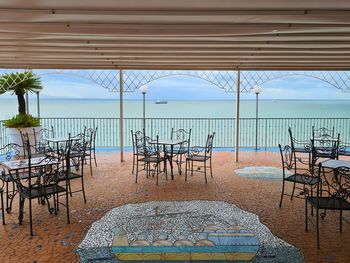 Empty chairs and table by sea against sky