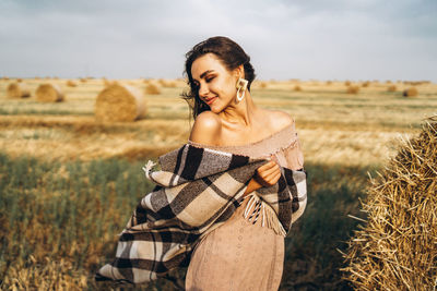 Smiling woman in sunglasses with bare shoulders on a background of wheat field and bales of hay.