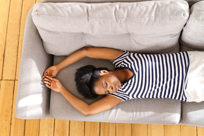 African american young woman wear stripped t-shirt resting, sleeping on couch with arms up at home