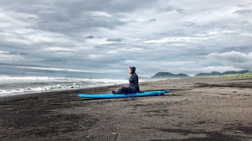 Full length of woman sitting on shore at beach against sky