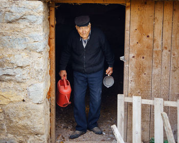 Portrait of man holding watering can and container while standing at entrance