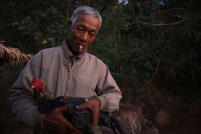 Mature man holding hen outdoors