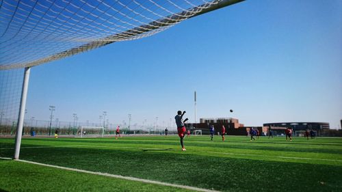 Players playing soccer on field against clear sky