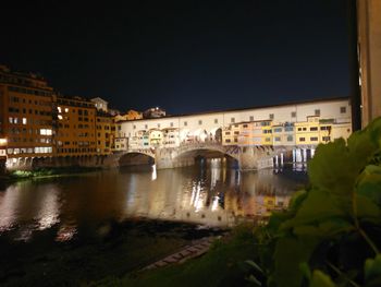 Arch bridge over river amidst buildings in city at night