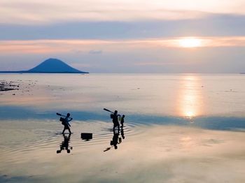 People on beach against sky during sunset