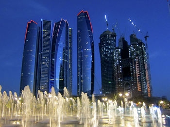 Low angle view of illuminated skyscrapers against blue sky at night