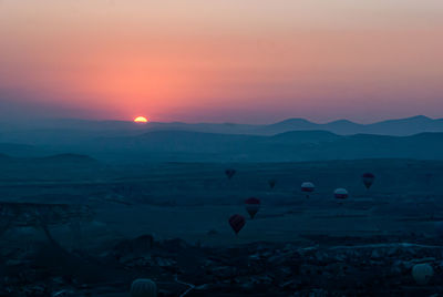 Scenic view of hot air balloons flying over landscape during sunset