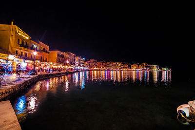 Illuminated buildings by river against sky at night