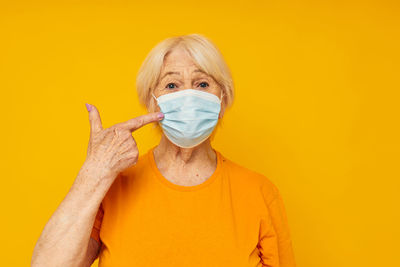 Portrait of senior woman wearing mask gesturing against yellow background