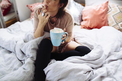 Midsection of woman sitting on bed at home