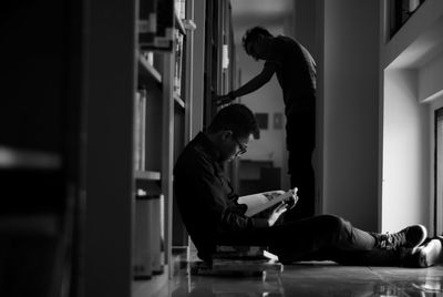 Side view of young man reading book while sitting on floor in library