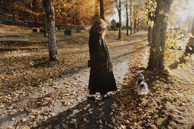 Full length side view of woman walking by dog at park during autumn
