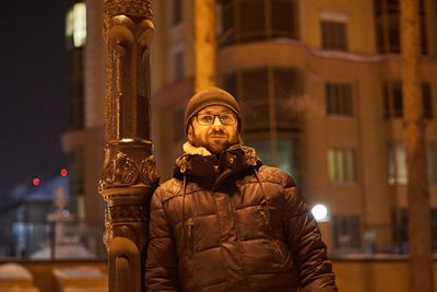 Portrait of man standing in city at night during winter