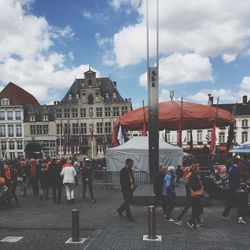 People walking in city against cloudy sky