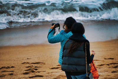 Rear view of woman photographing on beach