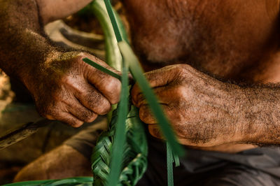 Midsection of shirtless man making leaves decoration